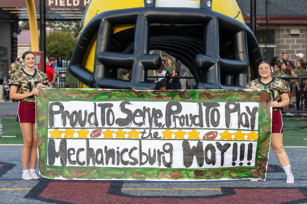 Cheerleaders holding sign for football players to run through.