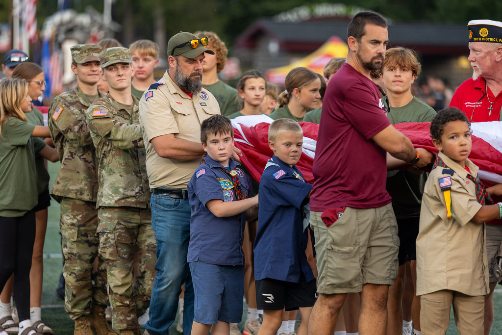 People lining a football field as they unravel a large American flag.