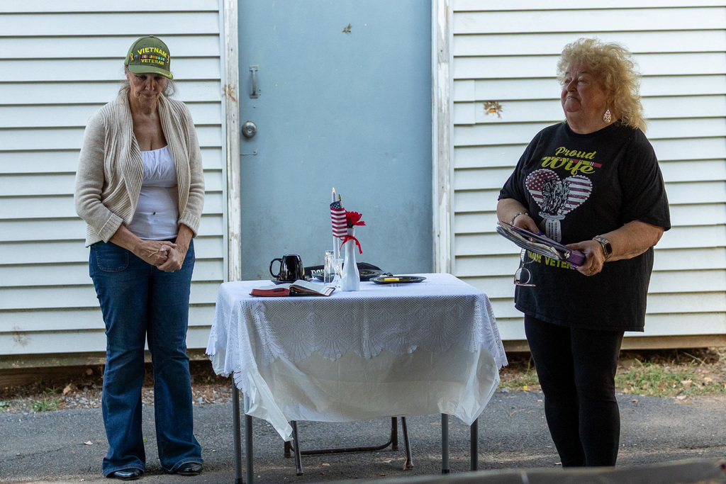 Volunteers standing at an empty table that signifies military personnel who have passed.