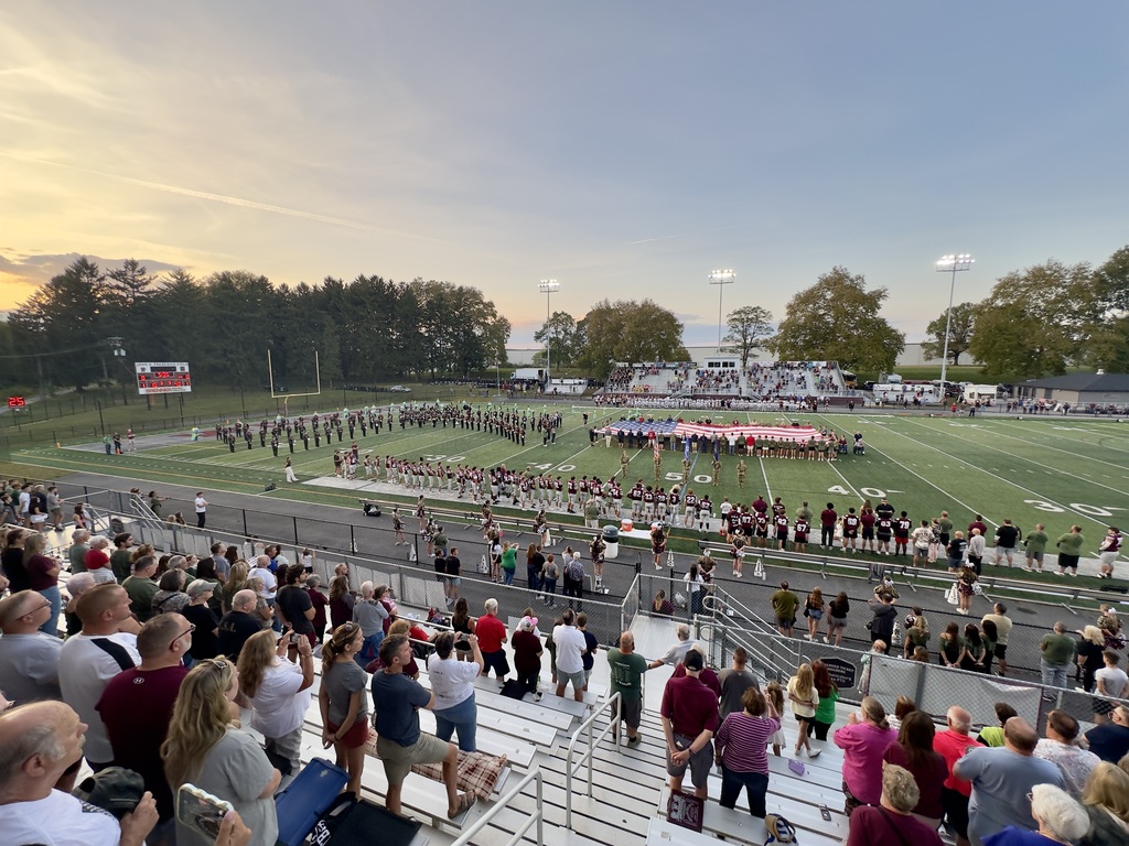 People lining a football field as they unravel a large American flag.