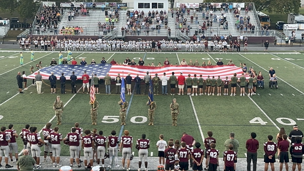 People lining a football field as they unravel a large American flag.