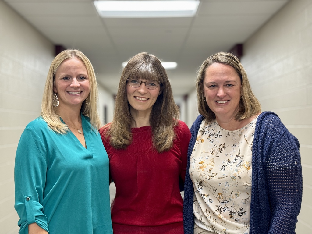 Three ladies standing arm in arm in a hallway.