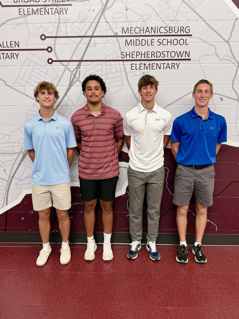A group of four young men standing next to each other in front of a painted cement wall.