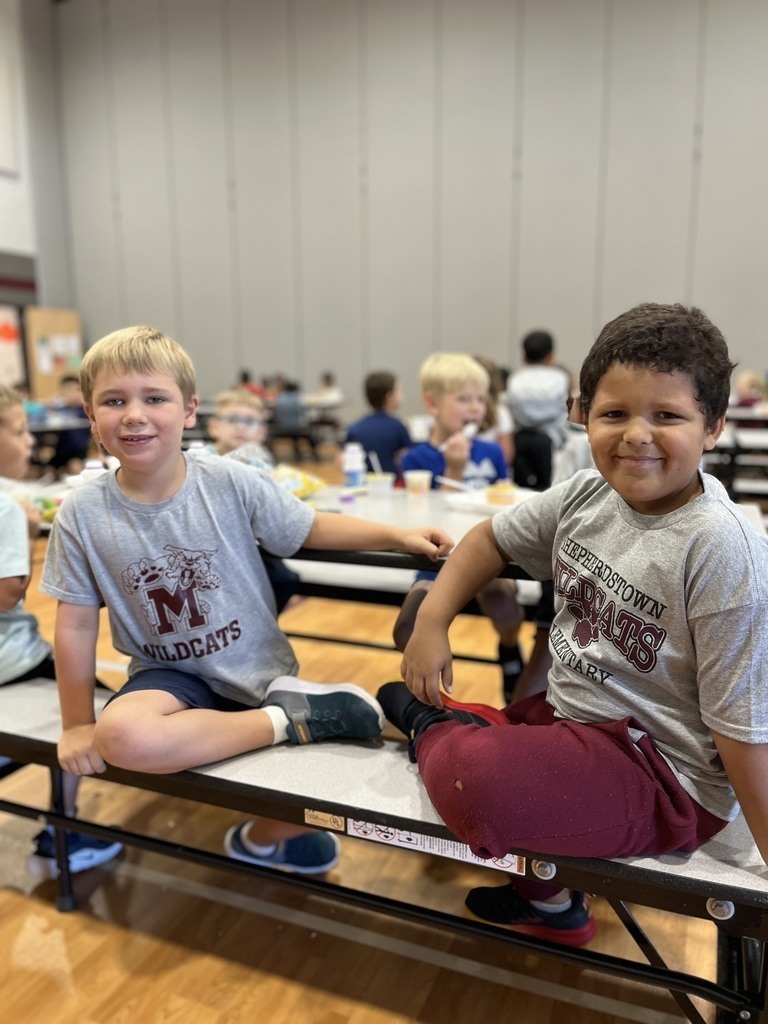 Two young boys at lunch showing off their school tshirts.