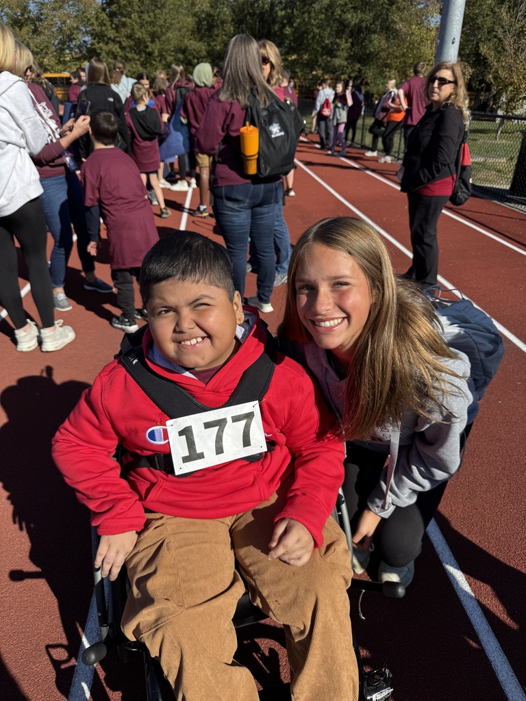 A student smiling with a little student in a wheelchair during special olympics.