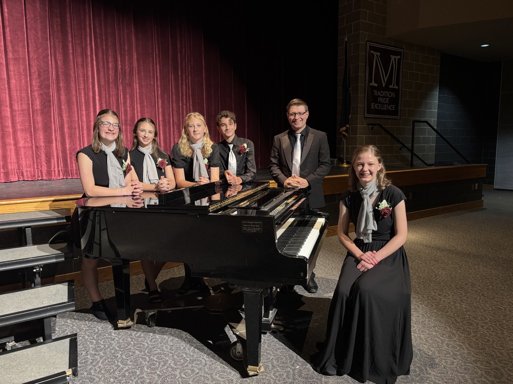 Group of student musicians standing around a piano.