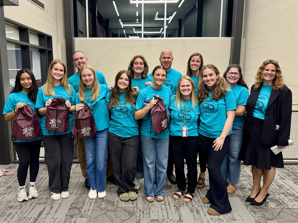 A group of students in teal tshirts standing with adult educators.