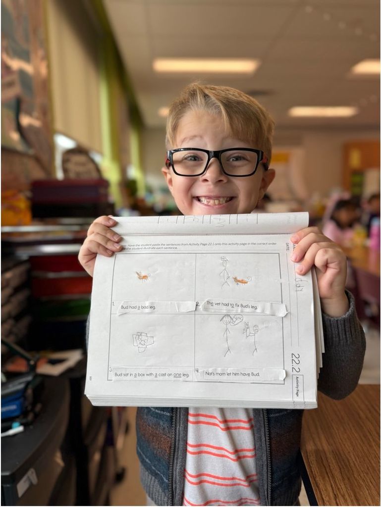 image of boy smiling, holding his school work