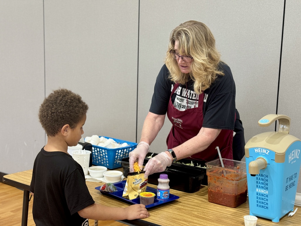 An adult putting cheese into a walking taco for a student.