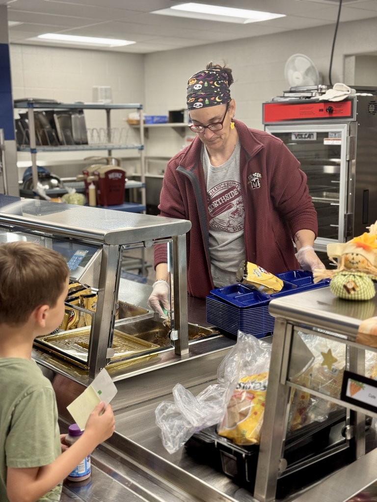 A staff member serving a young student his lunch.