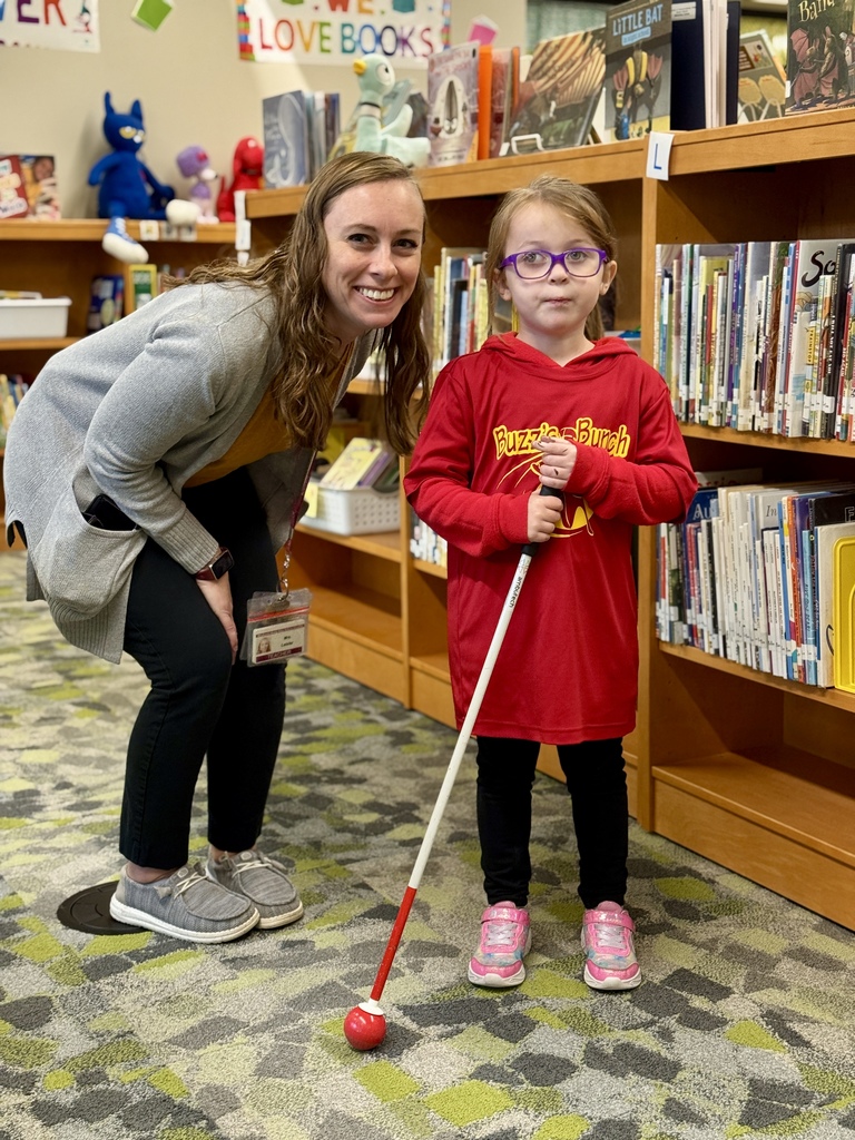 A young blind student standing beside a teacher with her white cane.