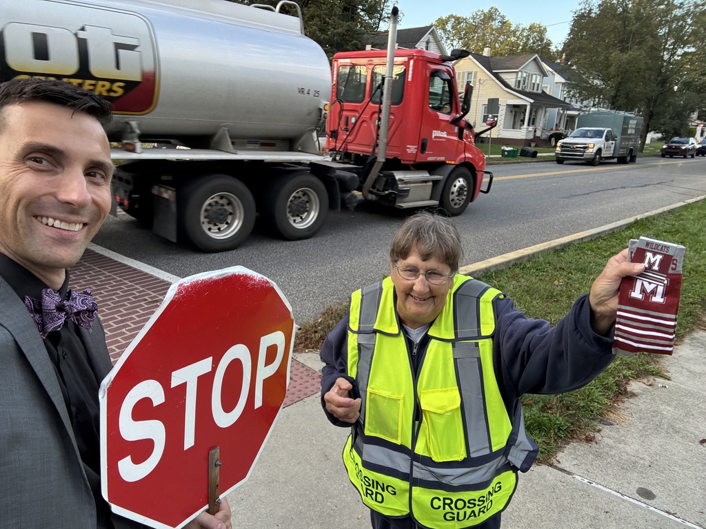 A man in a suit holding a stop sign while presenting a pair of branded socks to a school crossing guard.