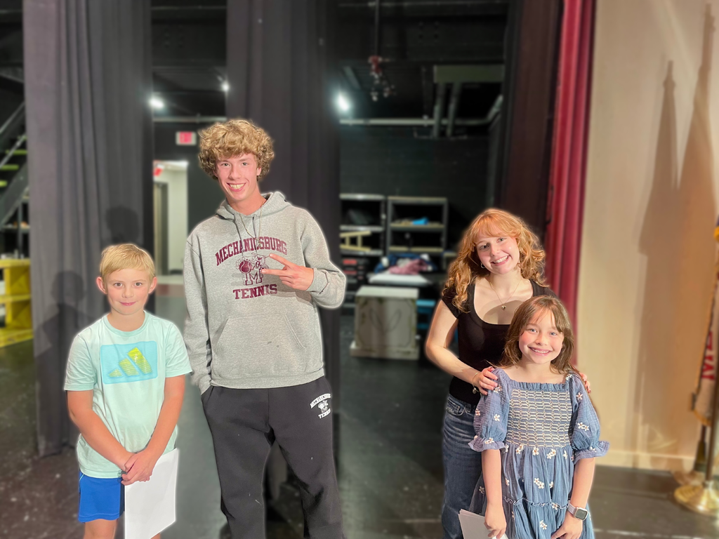 Two young students standing next to two older students backstage during play practice.