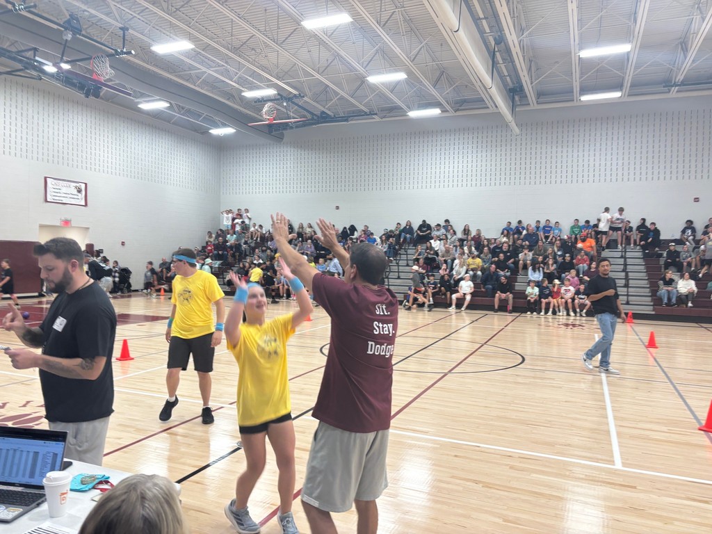A principal giving a high five to a student in a gym.