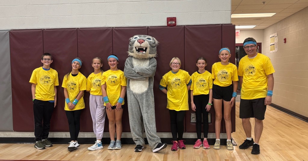 A group of students standing along a wall next to a Wildcat mascot.