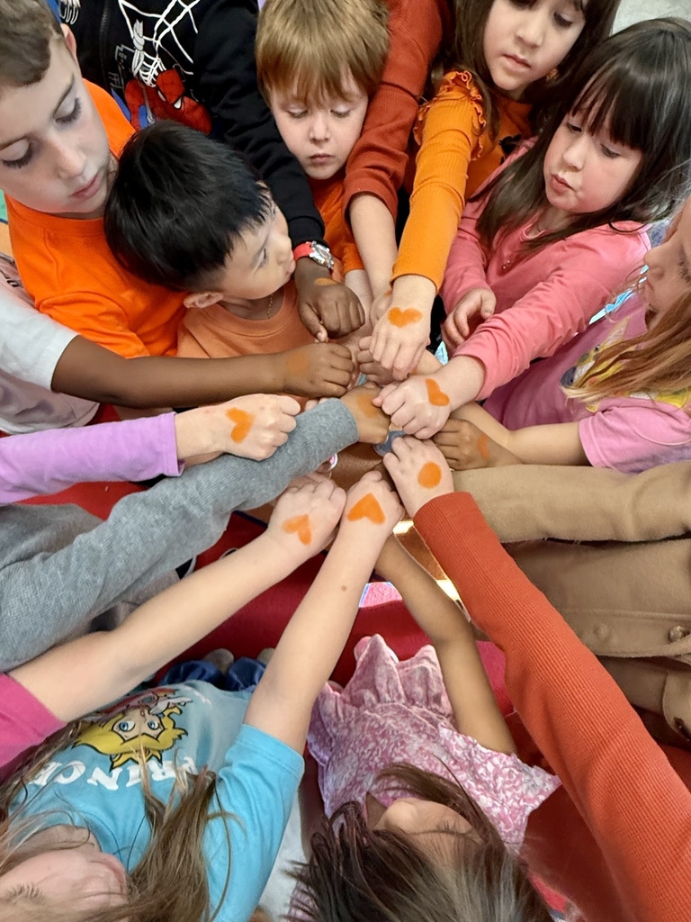 Students in orange, hands together showcasing an orange heart.