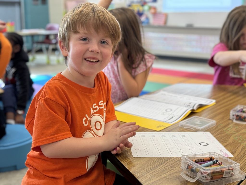 A young students in orange sitting at a desk.