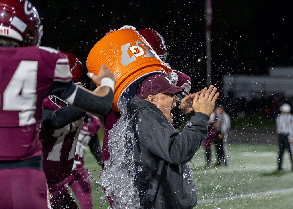 Football players on the field celebrating a win by dumping water on the coach