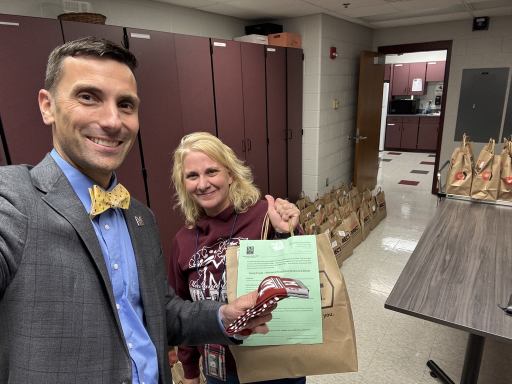 A man in a suit presents a female staff member with a pair of maroon Wildcats socks, while the staff member holds a weekend meal bag.