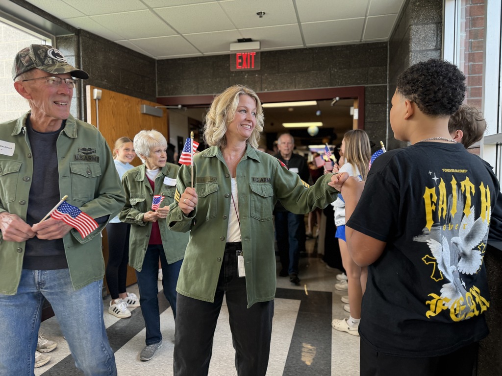 Veterans and families walking through hallways lined with students holding American flags.