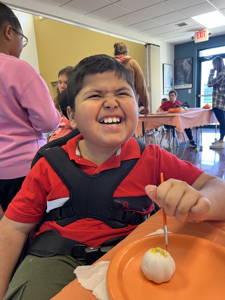 A student with a big smile, painting a small pumpkin.
