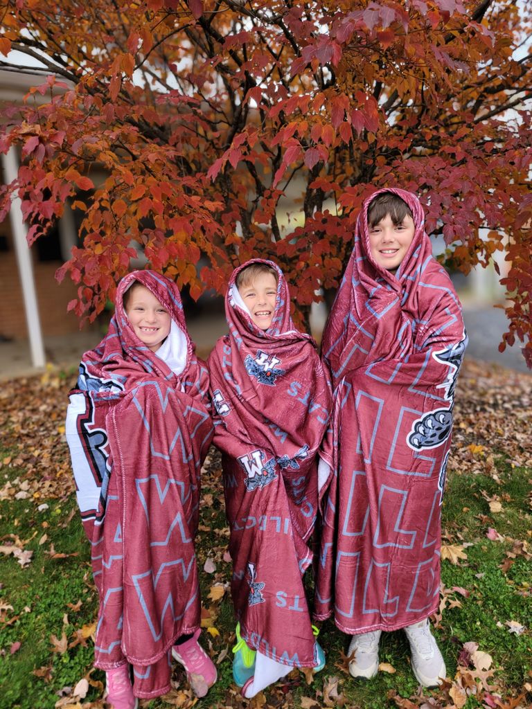 Three students cozied up with a warm and fuzzy maroon wildcat blanket.