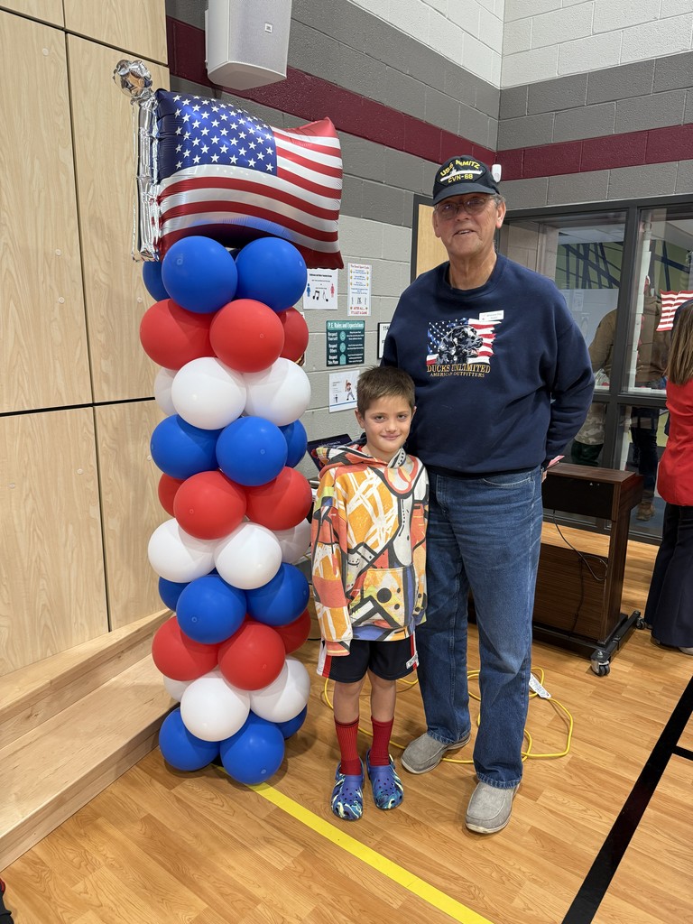 A student with a veteran standing next to red white and blue balloons.