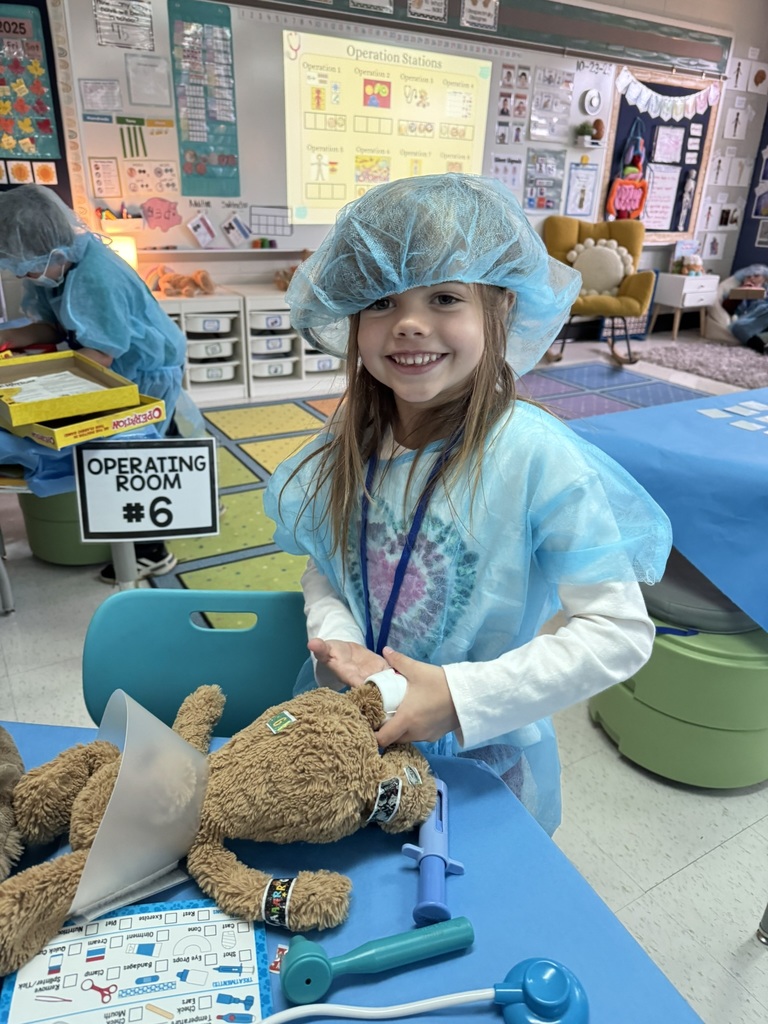 Student dressed as a play doctor, fixing a stuffed bear.