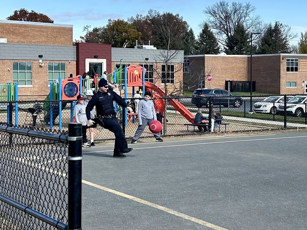 A police officer playing kickball on a playground with a group of students.
