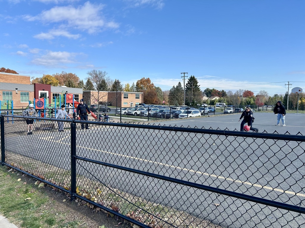 Police officers playing kickball on a playground with a group of students.