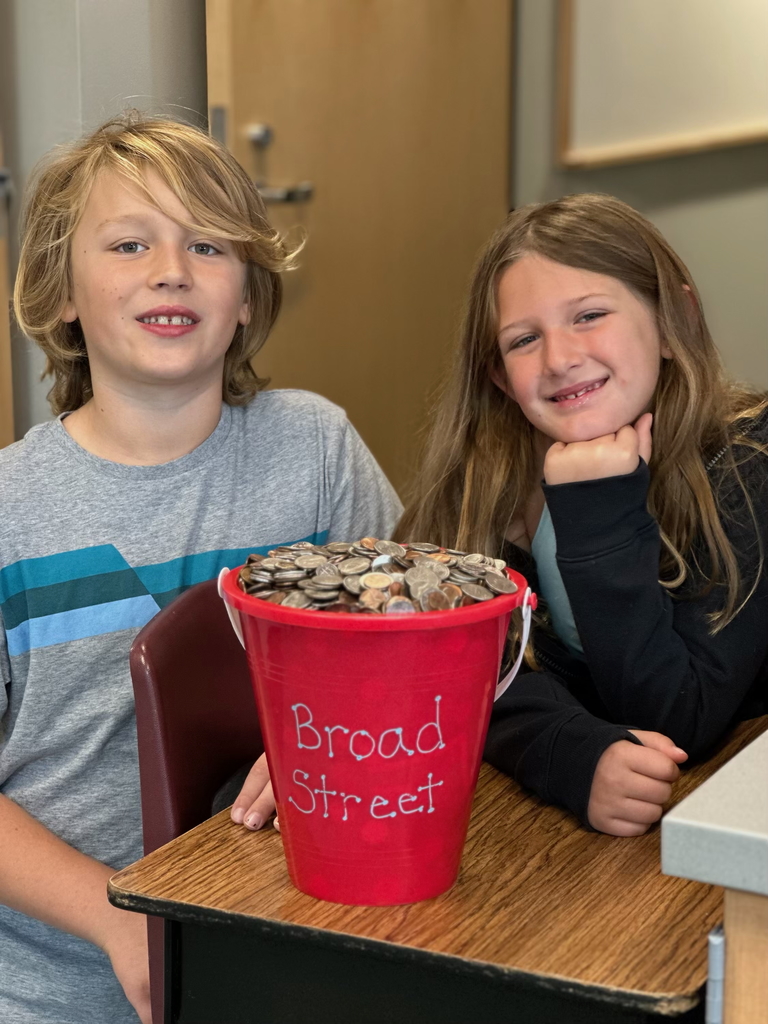 Two young students standing behind a bucket of coins that was donated for a fundraiser.