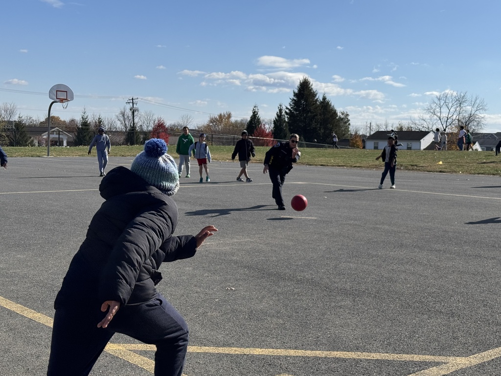 Students playing kickball on the playground with police officers.