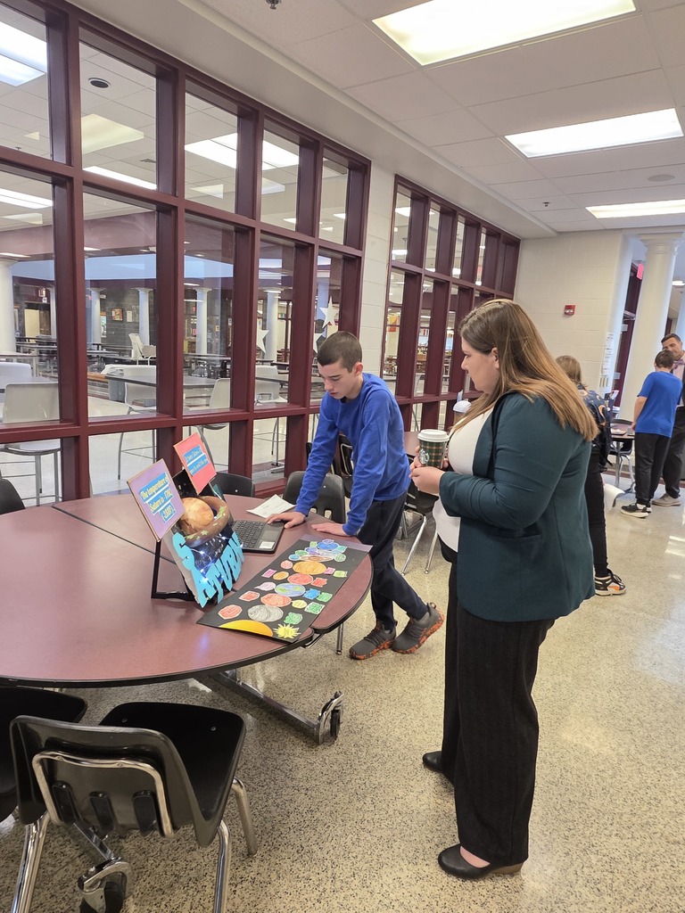 A student showing a teacher a display on the solar system.