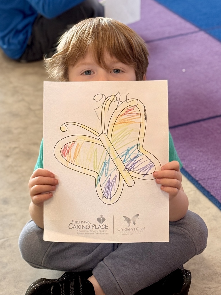 A young child proudly holding a picture of a butterfly they colored.