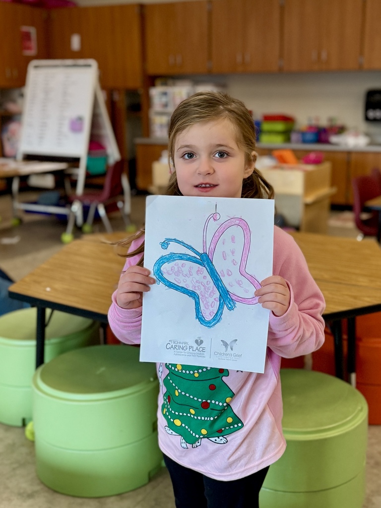 A young child proudly holding a picture of a butterfly they colored.