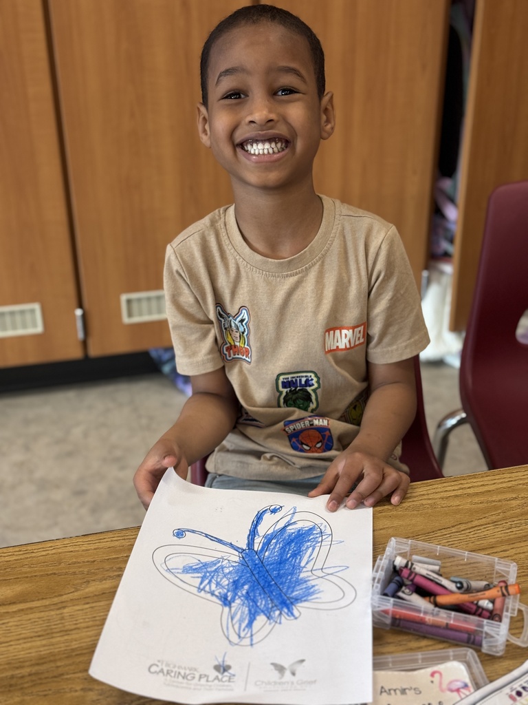 A young child proudly holding a picture of a butterfly they colored.