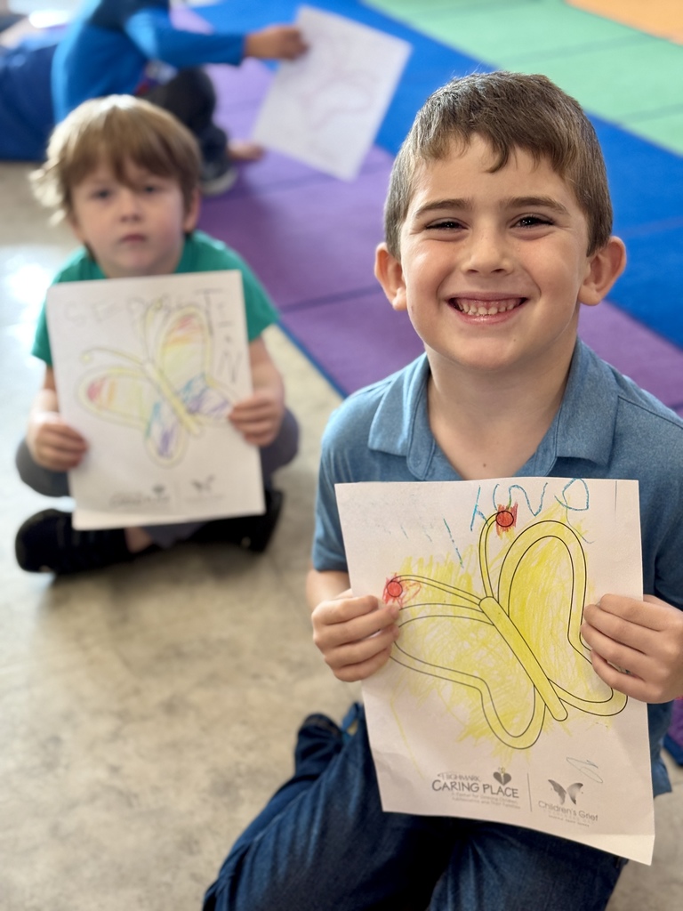 A young child proudly holding a picture of a butterfly they colored.