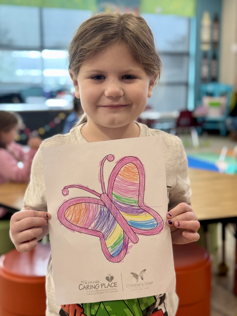 A young child proudly holding a picture of a butterfly they colored.
