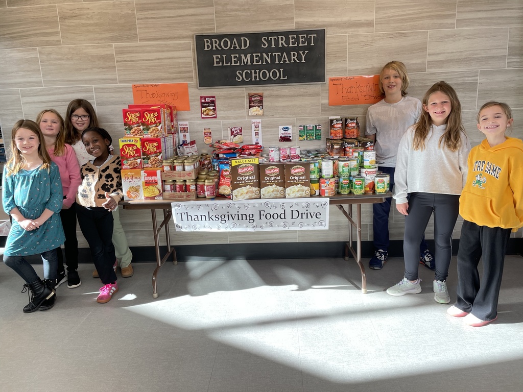 Students standing beside a table of food collected for a thanksgiving food drive.