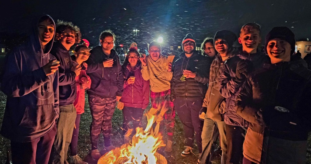 Students gathering around a campfire with hot chocolate in hand.