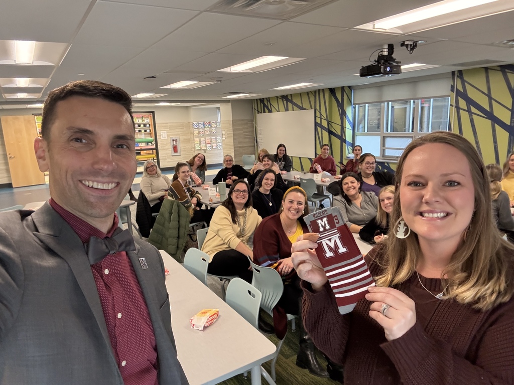 Man in suit presenting a pair of branded socks to a teacher while colleagues look on in the background.