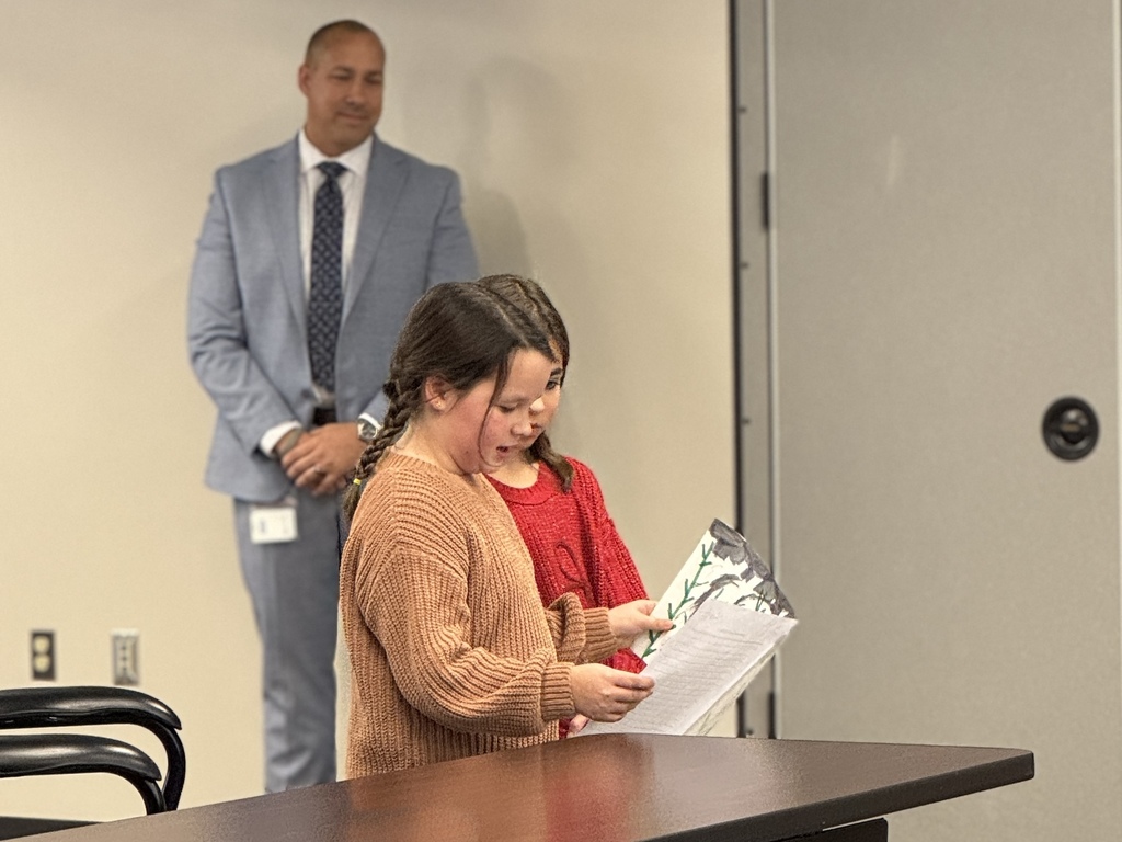 Two young girls reading a school project to school board members.
