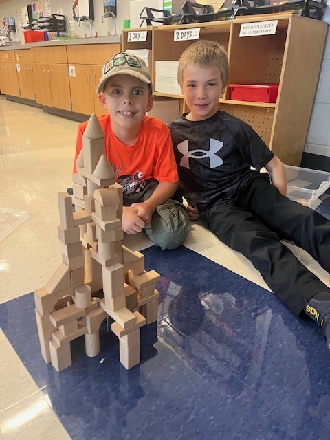 Two young boys with a tall tower of buidling blocks.