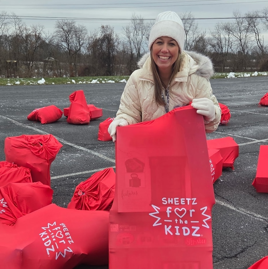 A lady in a white jacket holding a red bag full of holiday gifts.