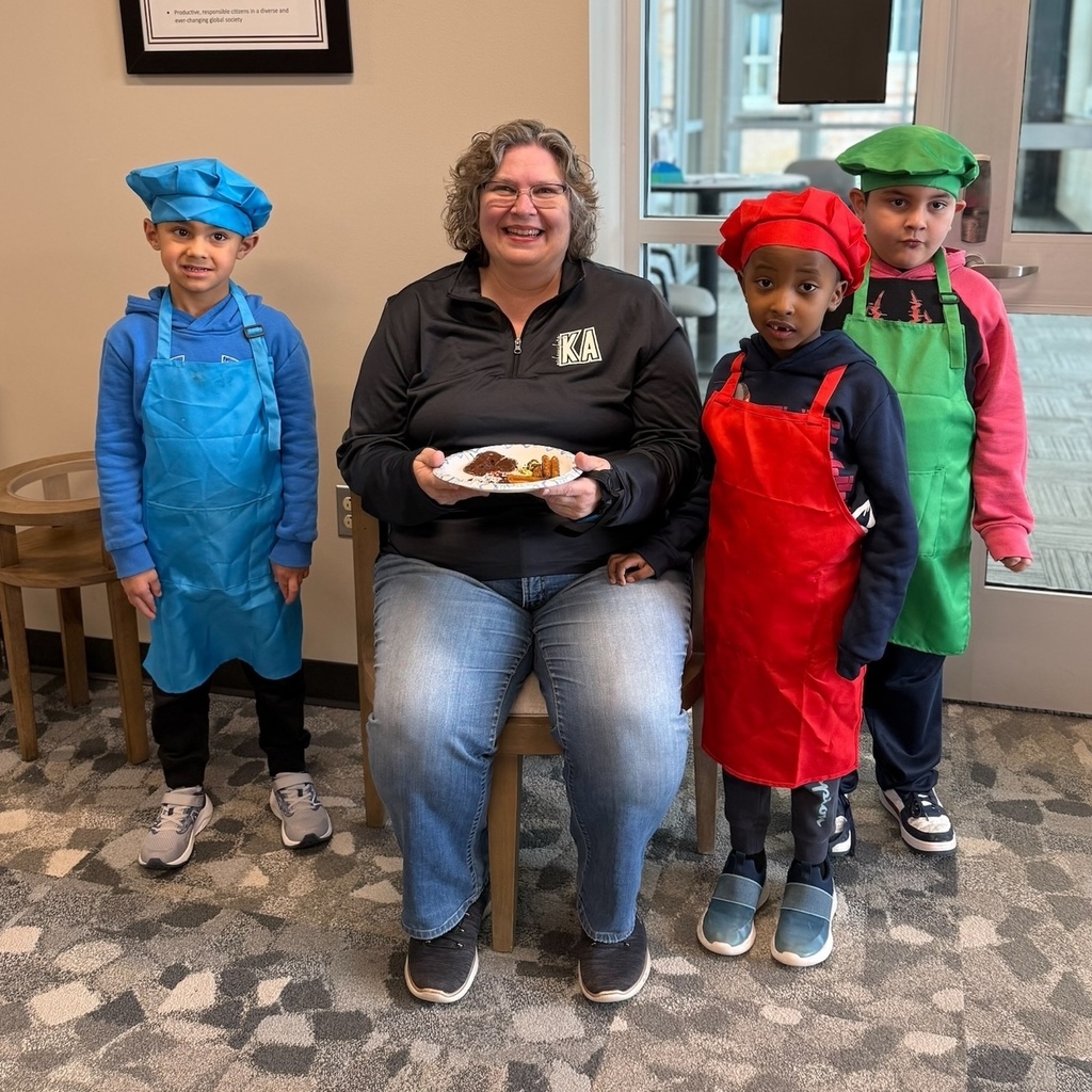 Young students in a chef's hat and aprons presenting a teacher with a plate of handmade treats.