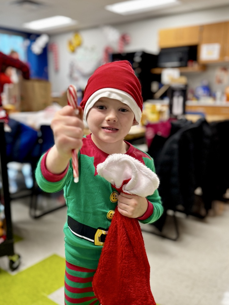young boy dressed as an elf holding out a candy cane