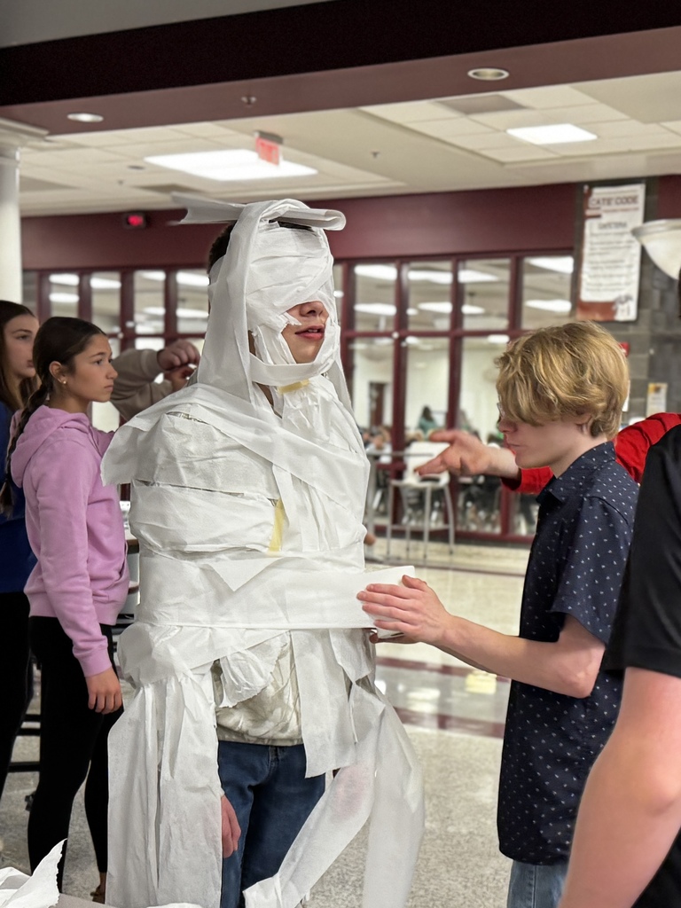 Students wrapping a classmate in toilet paper for a Build A Snowman STEM challenge.