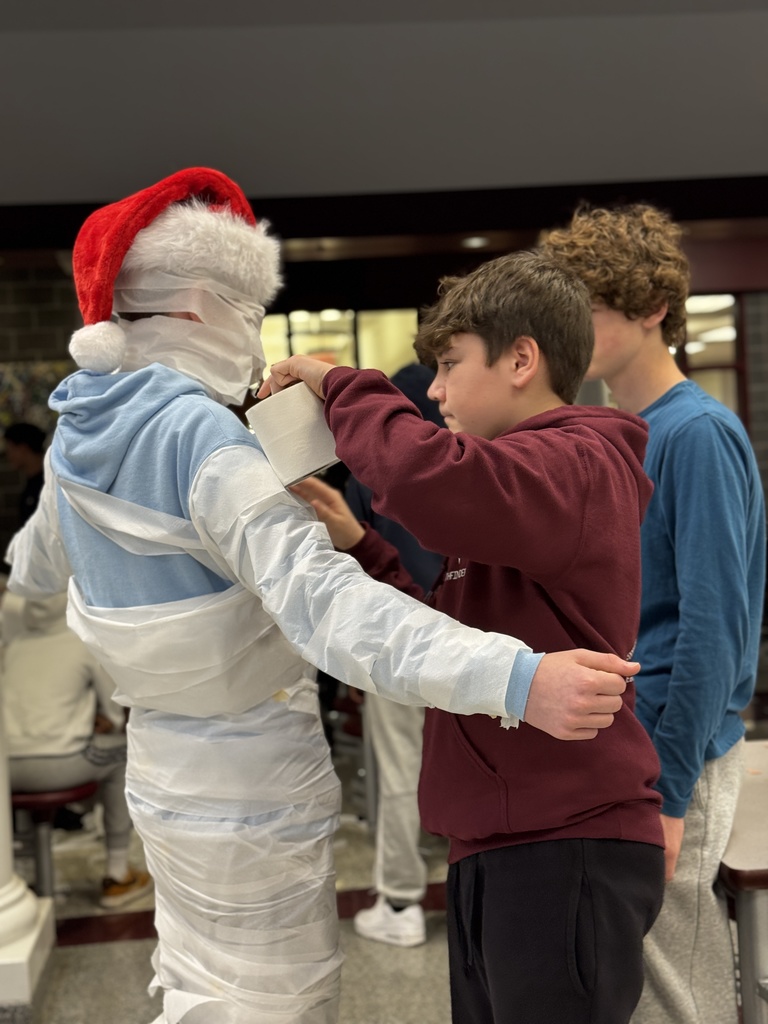 Students wrapping a classmate in toilet paper for a Build A Snowman STEM challenge.