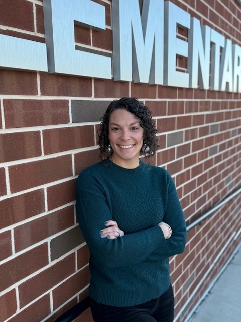 Headshot of new school principal standing along a brick wall.