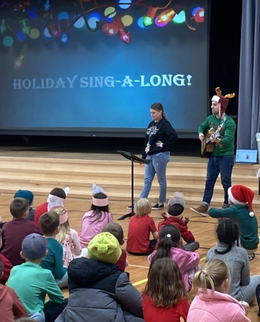 Staff perform holiday songs for a crowd of students.